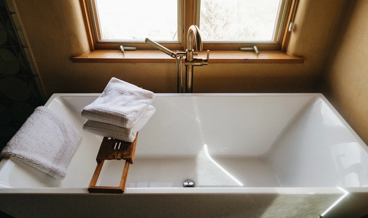 Folded towels on a wooden tray across a white bathtub