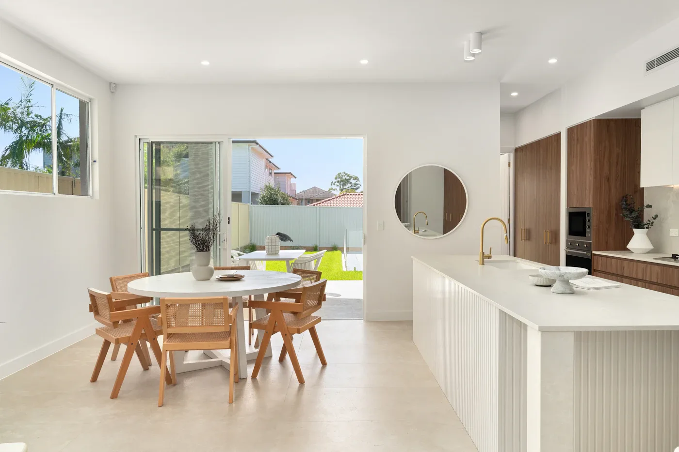 Round wooden dining table beside a bright white kitchen