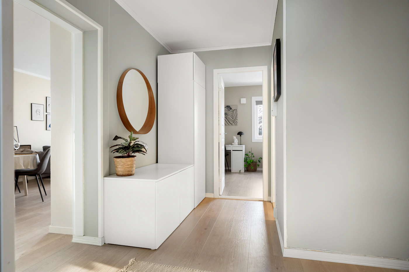 White hallway storage with a round mirror and potted plant