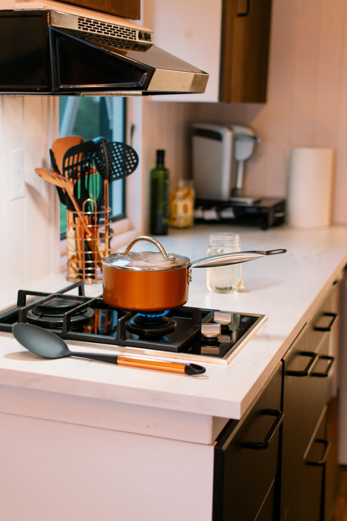 Orange saucepan and cooking utensils beside a kitchen stove